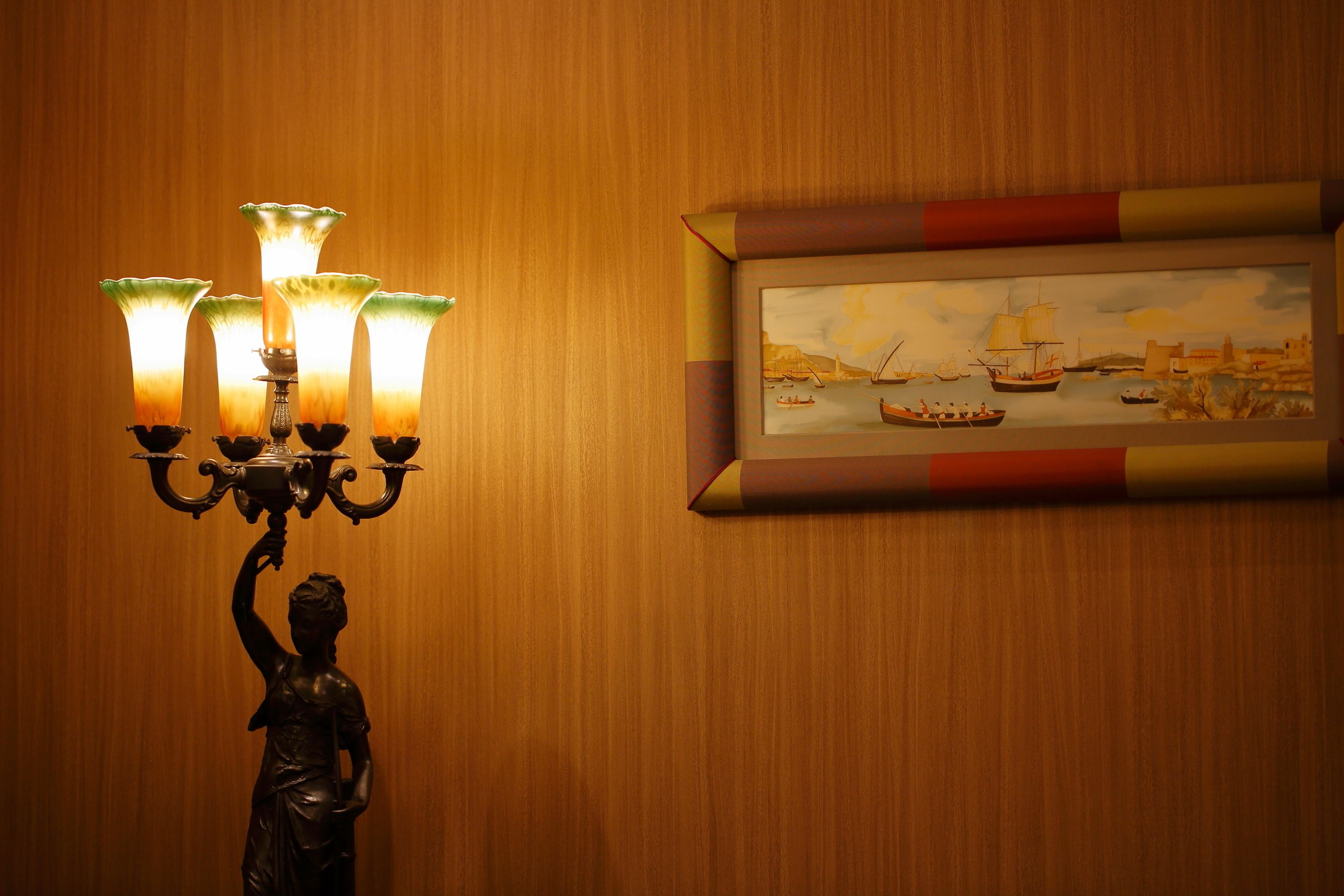 A wall-mounted painting of a coastal scene with ships, a framed picture, and a wall-mounted candelabra with lit candles.