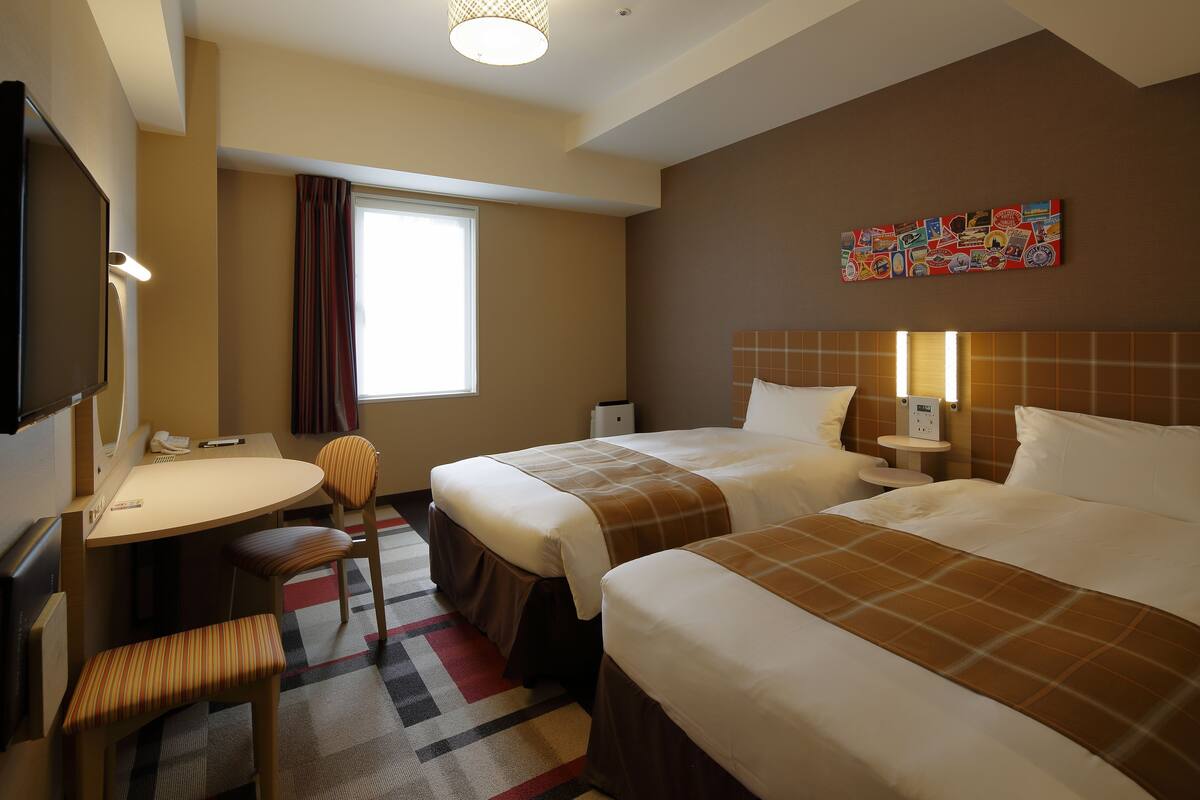 Une chambre d’hôtel avec deux lits, un bureau, une chaise et un téléviseur.
