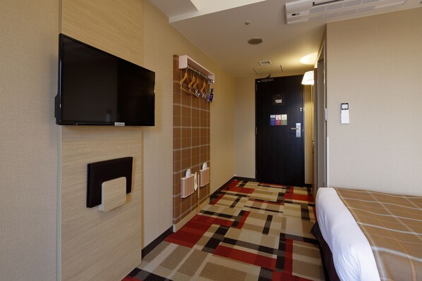 Una habitación de hotel con cama, televisor en la pared, perchero y mostrador de recepción.