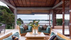 Un espacio exterior moderno con dos sofás acolchados, una mesa de centro de madera y vistas a un lago.