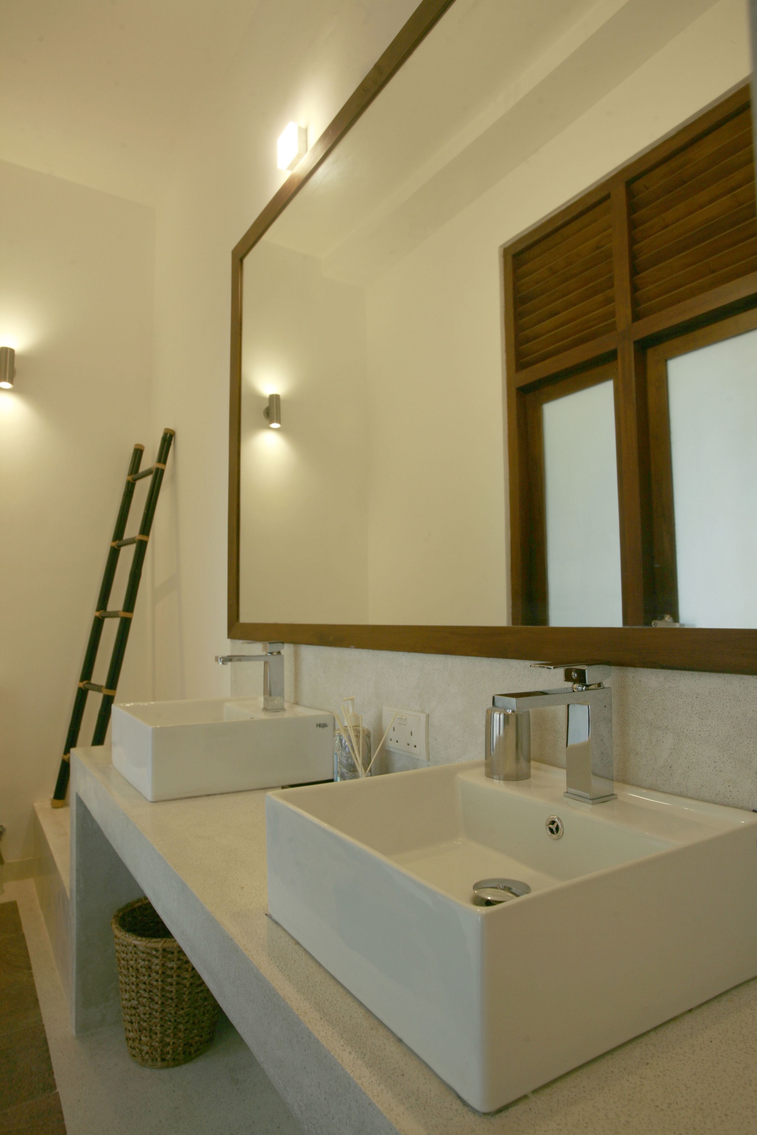A bathroom with two white sinks, a large mirror, and a wooden ladder leaning against the wall.