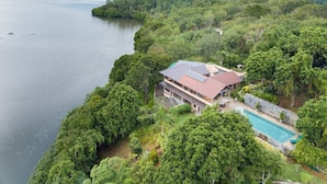 Una casa grande con piscina, rodeada de un bosque denso y un lago.