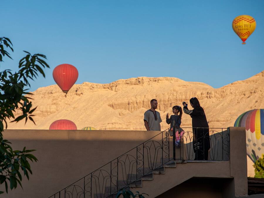 A balcony with a view of a desert landscape and hot air balloons in the background.