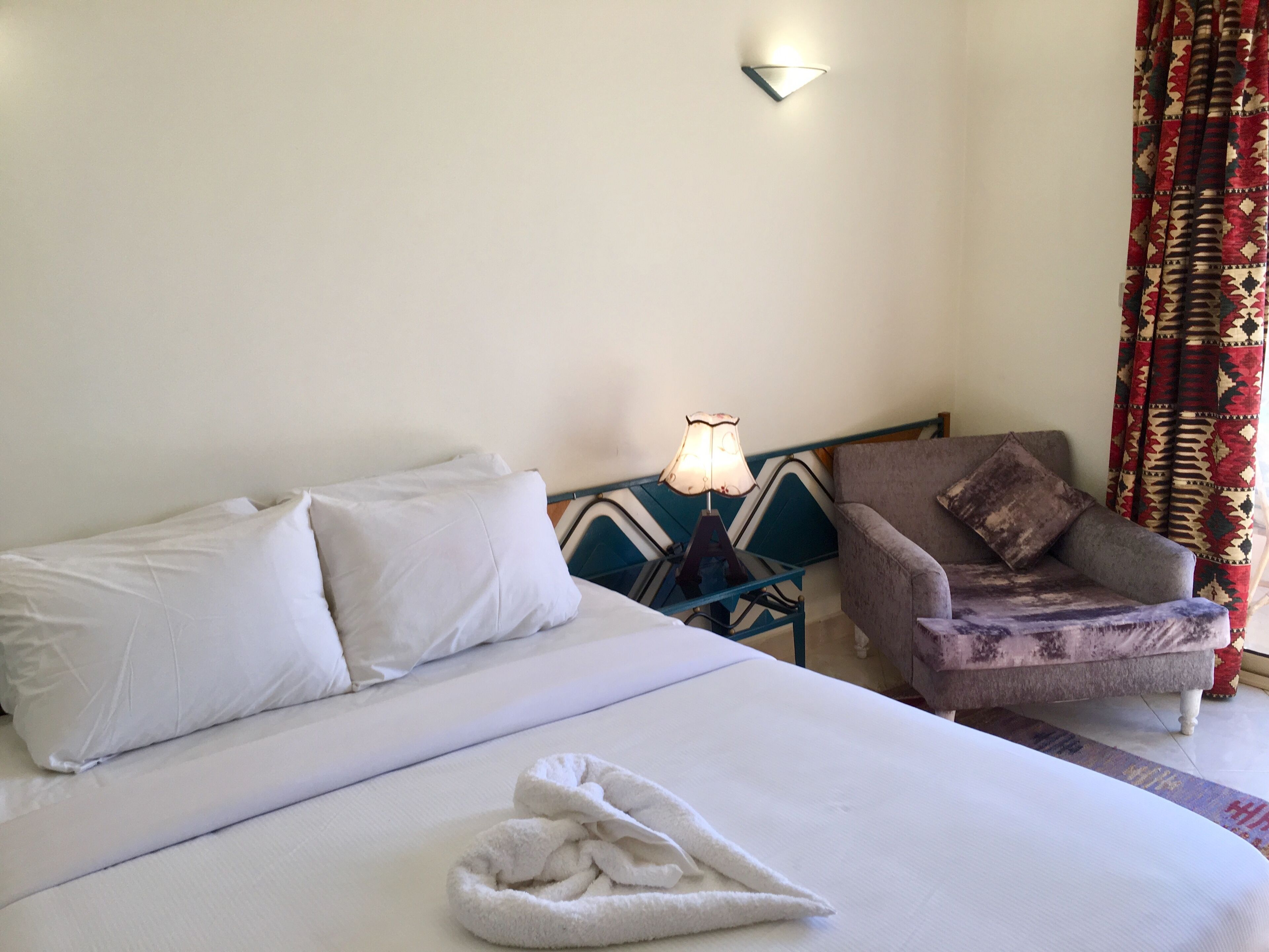 A hotel room with a bed, a chair, a lamp, and a curtain.
