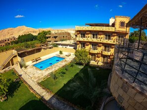 A hotel with a swimming pool, outdoor seating, and a view of the surrounding landscape. - New Memnon Hotel (Luxor)