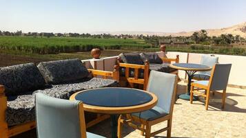 Un espacio al aire libre con sofá y sillones, una mesa redonda, y vistas a un campo verde y colinas lejanas.