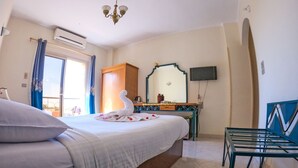 Habitación de hotel con cama, escritorio, silla, televisor y ventana con cortinas.