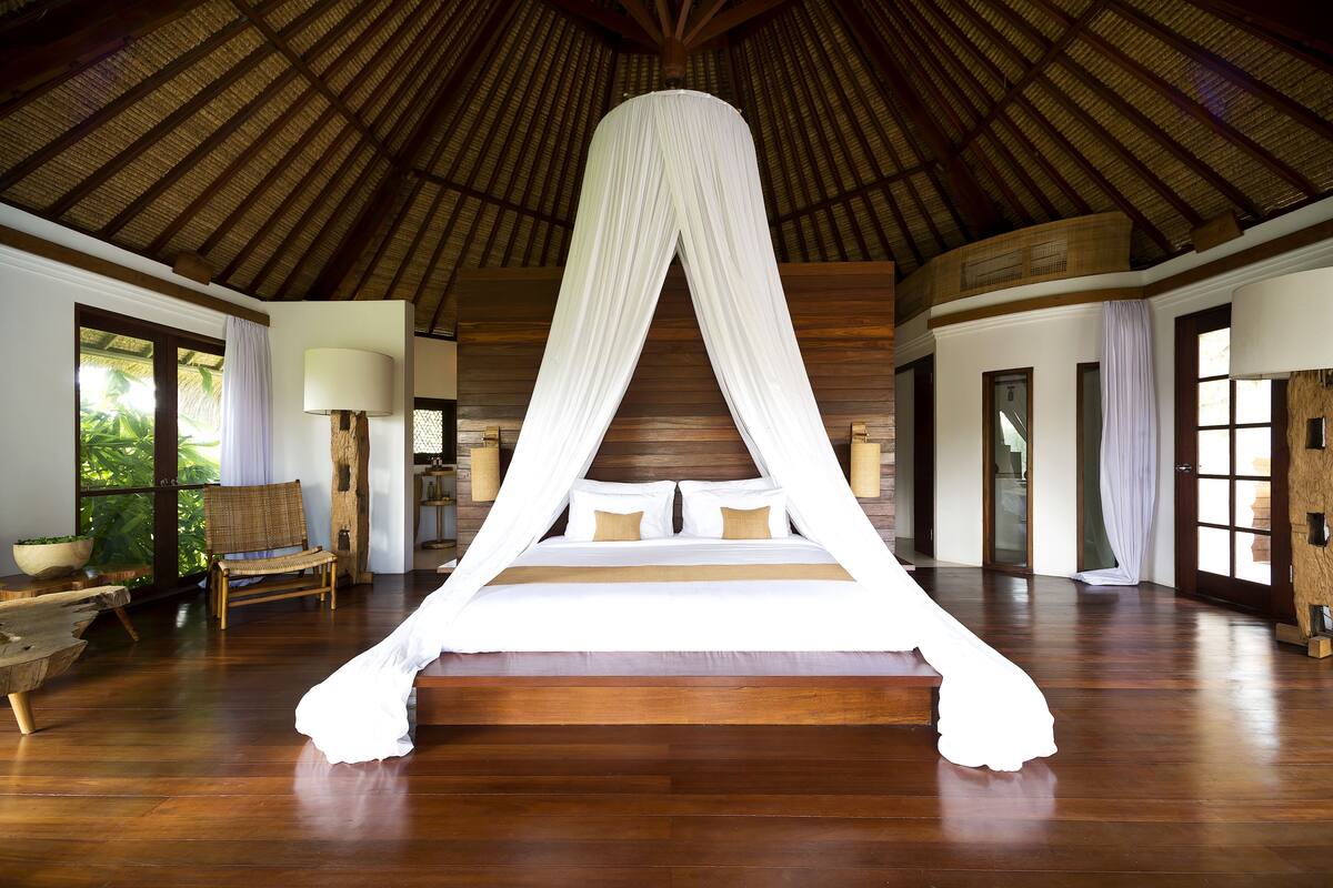Una cama grande con dosel en una habitación amplia con pisos de madera y ventanas grandes.
