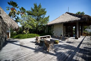 Una terraza de madera con mobiliario exterior, una estructura de techo de paja y abundante vegetación.