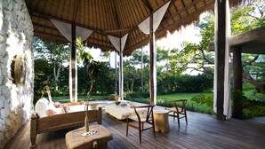 A wooden deck with a thatched roof, a wooden bench, and a table with chairs.