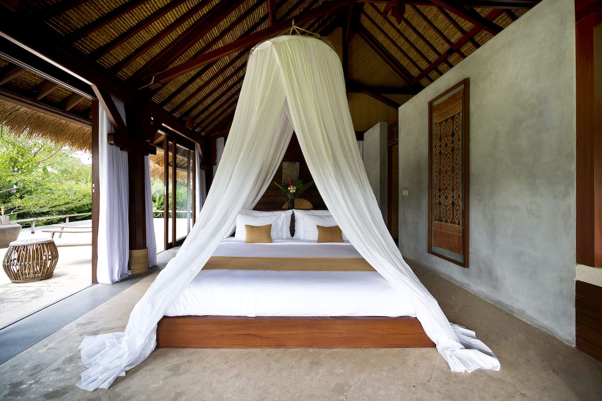 Una cama con dosel, suelo de madera y vistas a la vegetación.