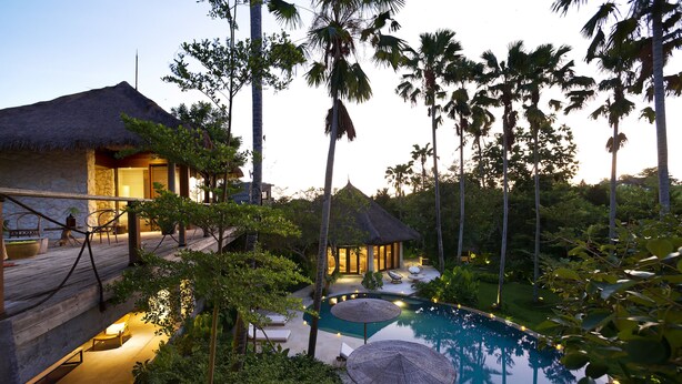 A resort with a swimming pool, lounge chairs, and thatched-roof structures.