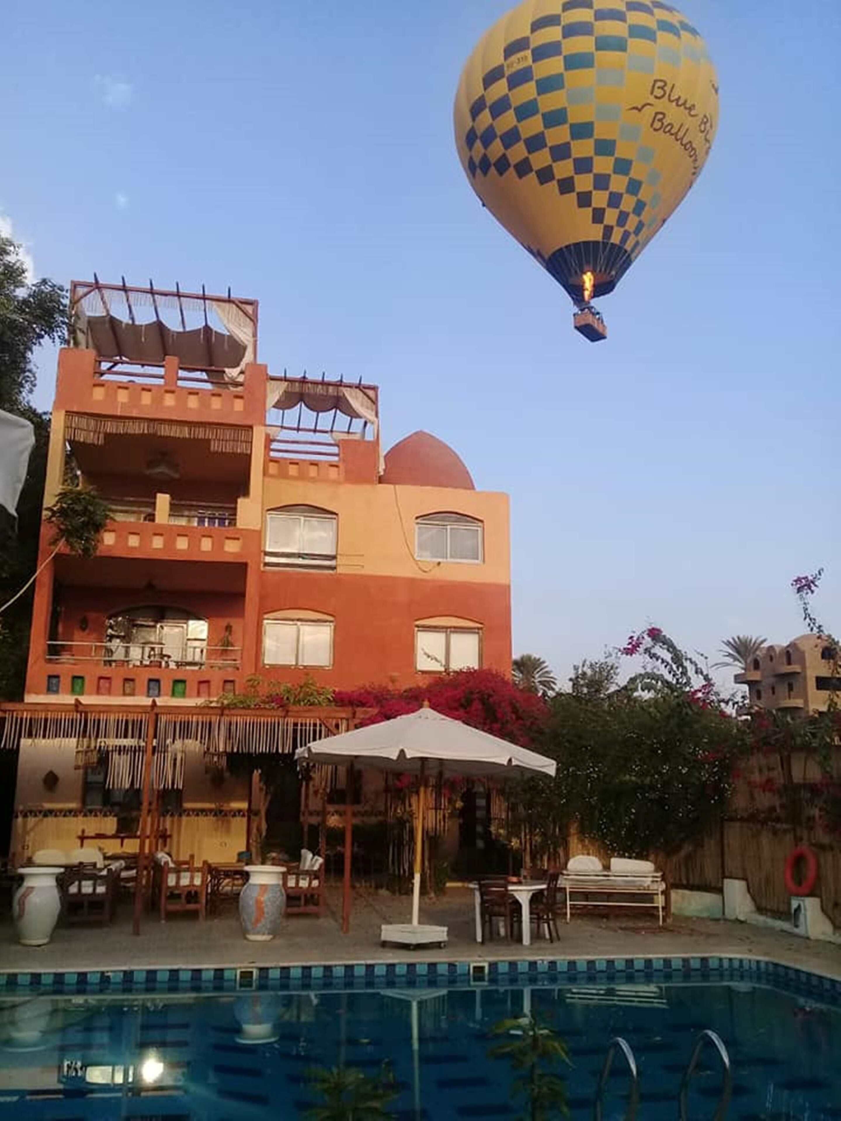 A hotel with a pool, outdoor seating, and a hot air balloon in the background.
