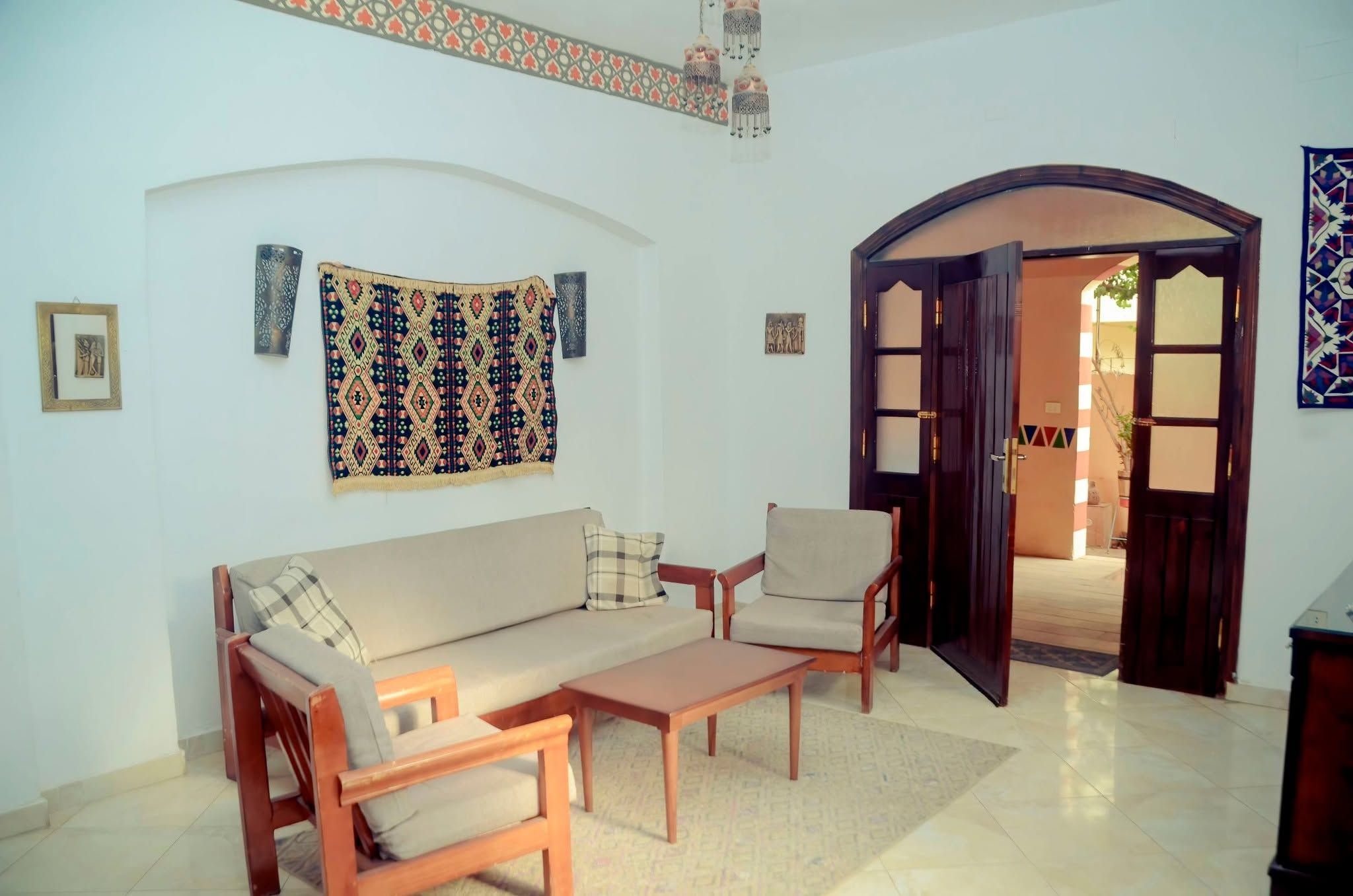 A living room with a sofa, two armchairs, a coffee table, and a patterned tapestry.