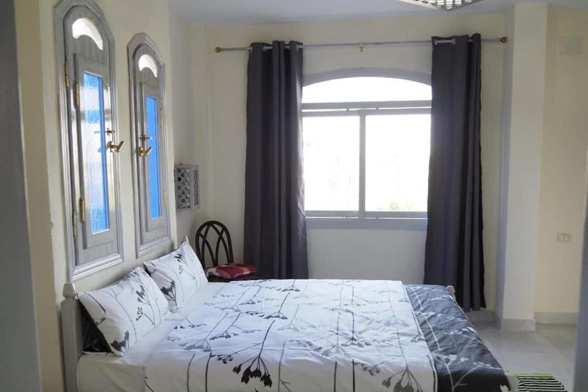 A bedroom with a bed, two windows with curtains, and a chair.
