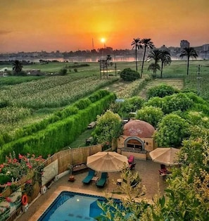 Un resort con piscina, tumbonas y vistas a un campo de arroz al atardecer.
