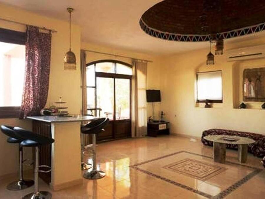 Una sala de estar con un sofá, una mesa de centro, una zona de bar con taburetes, un televisor y una alfombra estampada.