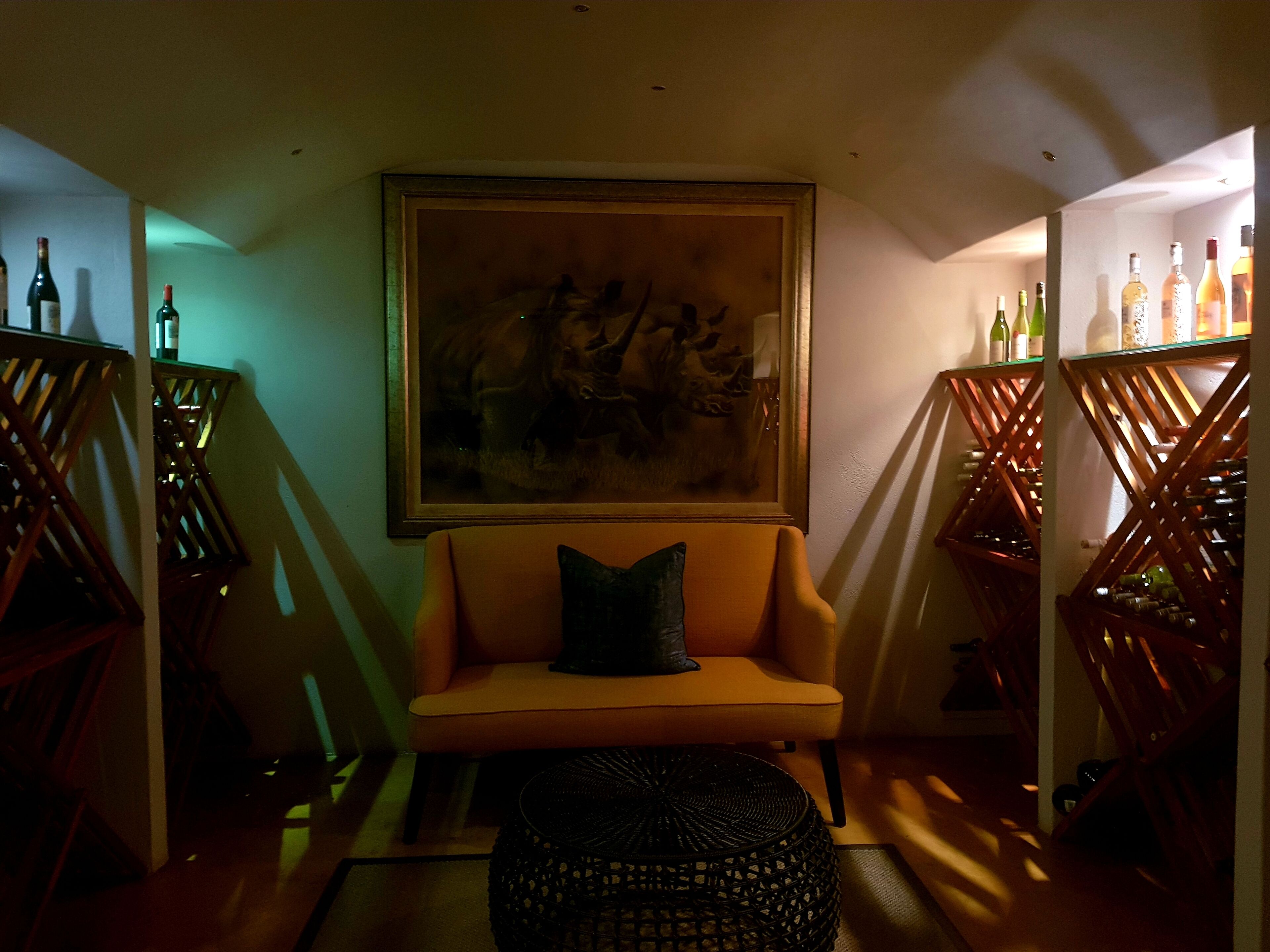 Um quarto com pouca luz, um sofá, um quadro emoldurado e duas estantes de madeira para vinho.