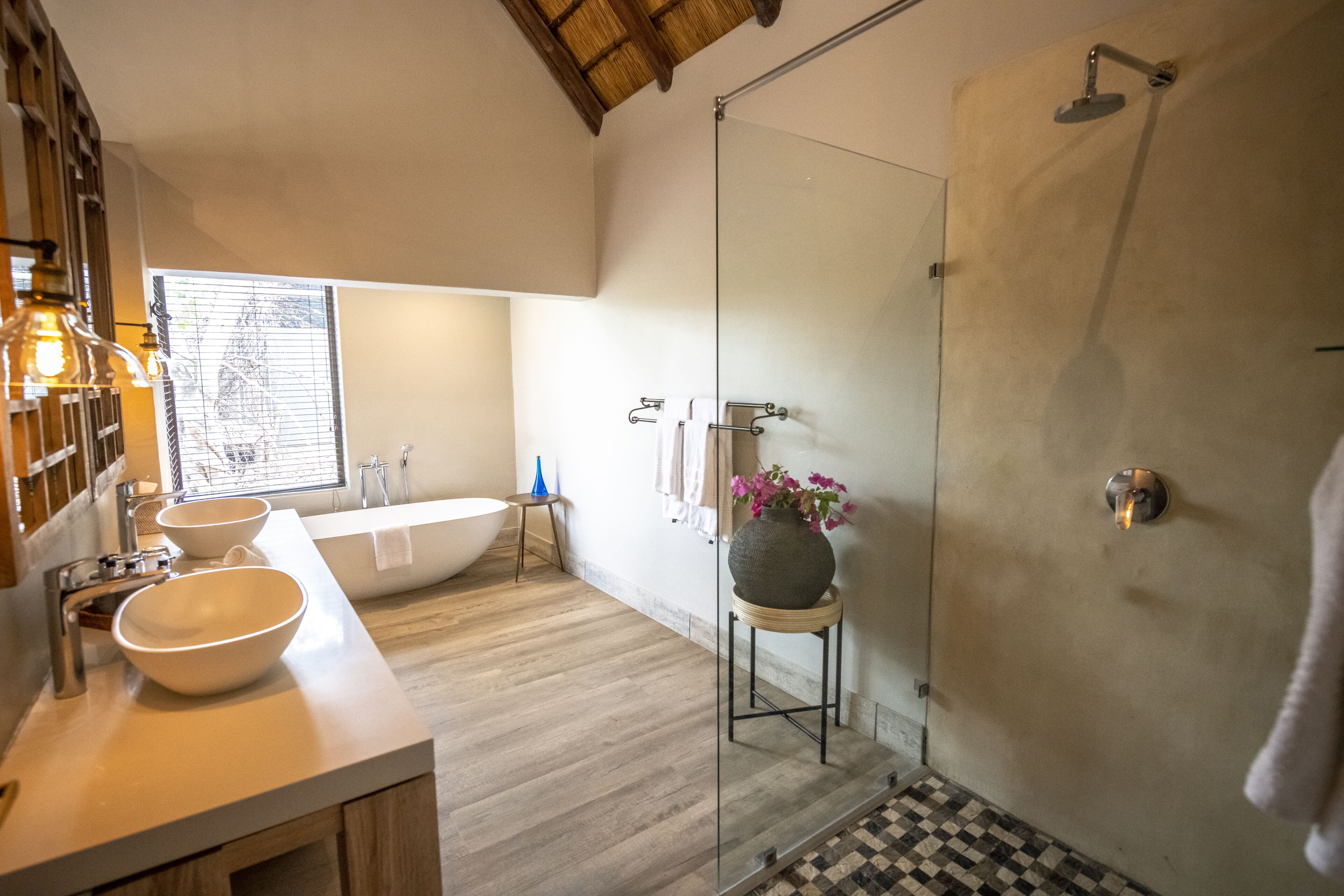 A modern bathroom with a large bathtub, a glass-enclosed shower, and a wooden vanity with two bowls.