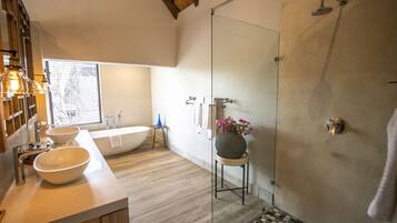 Ein modernes Badezimmer mit einer großzügigen Badewanne, einer in Glas eingefassten Dusche und einem hölzernen Waschtisch mit zwei Becken.