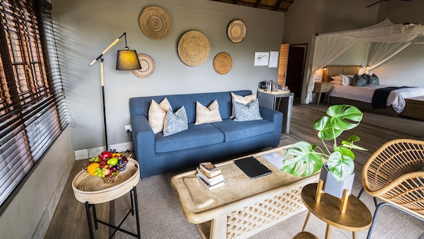 A room with a blue sofa, a coffee table, a wicker chair, a bedside table with a lamp, and a bed with a canopy.