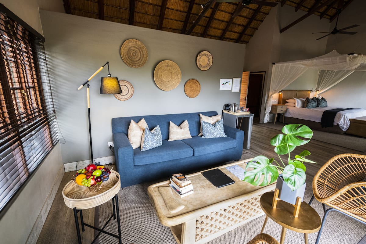 Une pièce avec un canapé bleu, une table basse, un fauteuil en osier, une table de chevet avec une lampe et un lit à baldaquin.