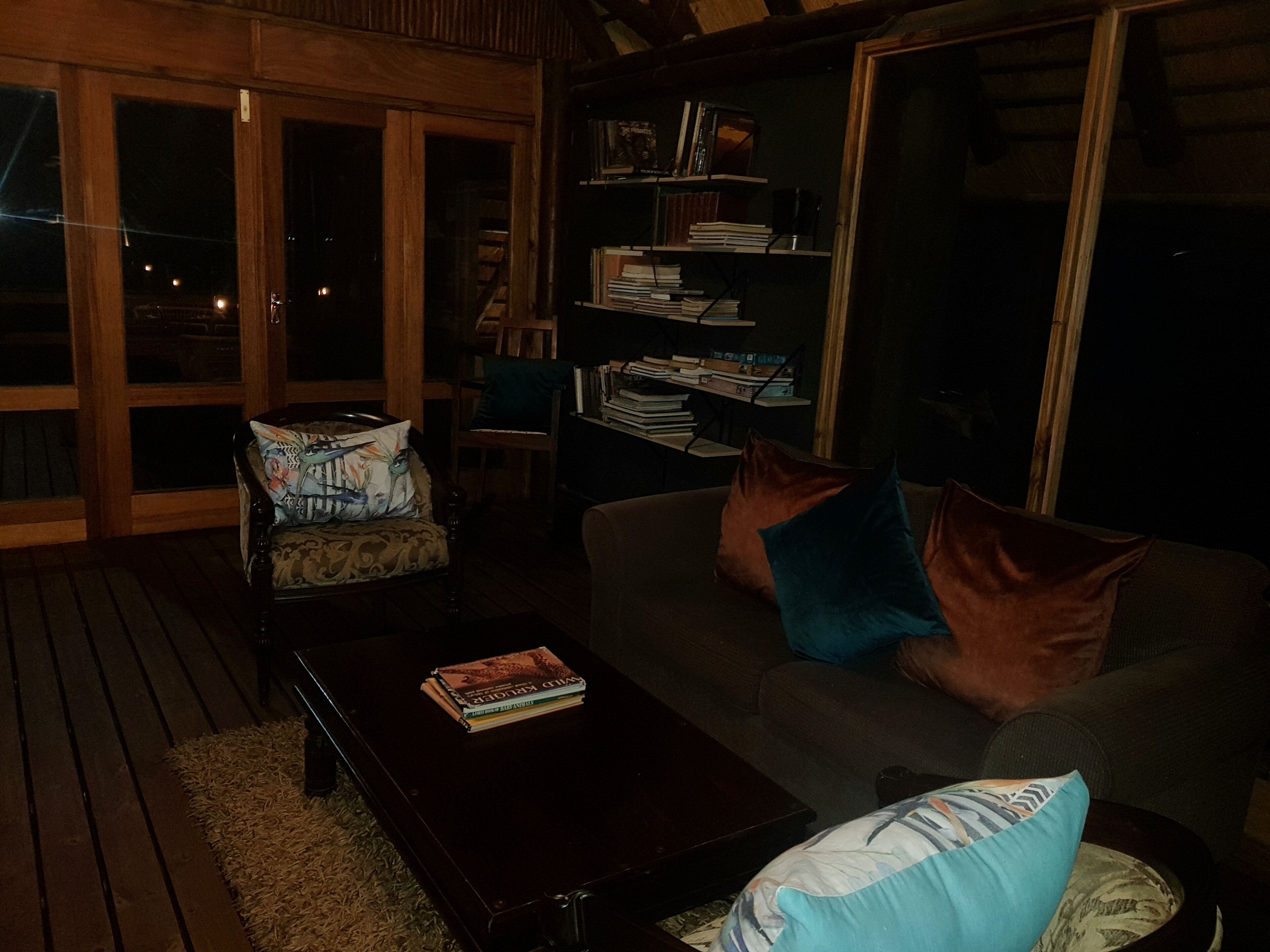 A cozy living room with a sofa, armchairs, and a coffee table. There is a bookshelf filled with books and a window with a view.
