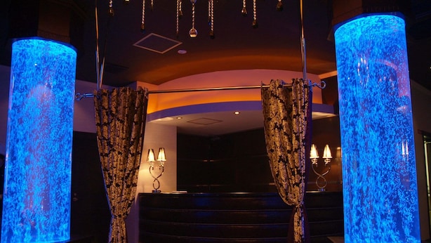 A lobby with two large illuminated columns, a staircase, and a reception desk with three lit lamps. - Hotel Mint - Adults Only (Ikeda)