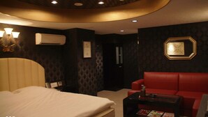 A hotel room with a bed, a red sofa, a small table, and a wall-mounted air conditioner. - Hotel Mint - Adults Only (Ikeda)