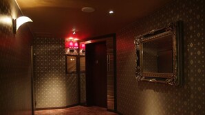 A hallway with patterned wallpaper, a large ornate mirror, and a red-lit lamp. - Hotel Mint - Adults Only (Ikeda)