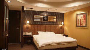 A hotel room with a large bed, two bedside lamps, a mirror above the bed, a framed picture on the wall, and a trash bin. - Hotel Mint - Adults Only (Ikeda)
