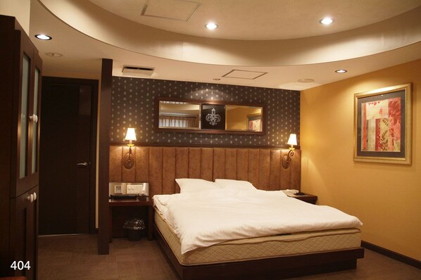 A hotel room with a large bed, two bedside lamps, a mirror above the bed, a framed picture on the wall, and a trash bin.