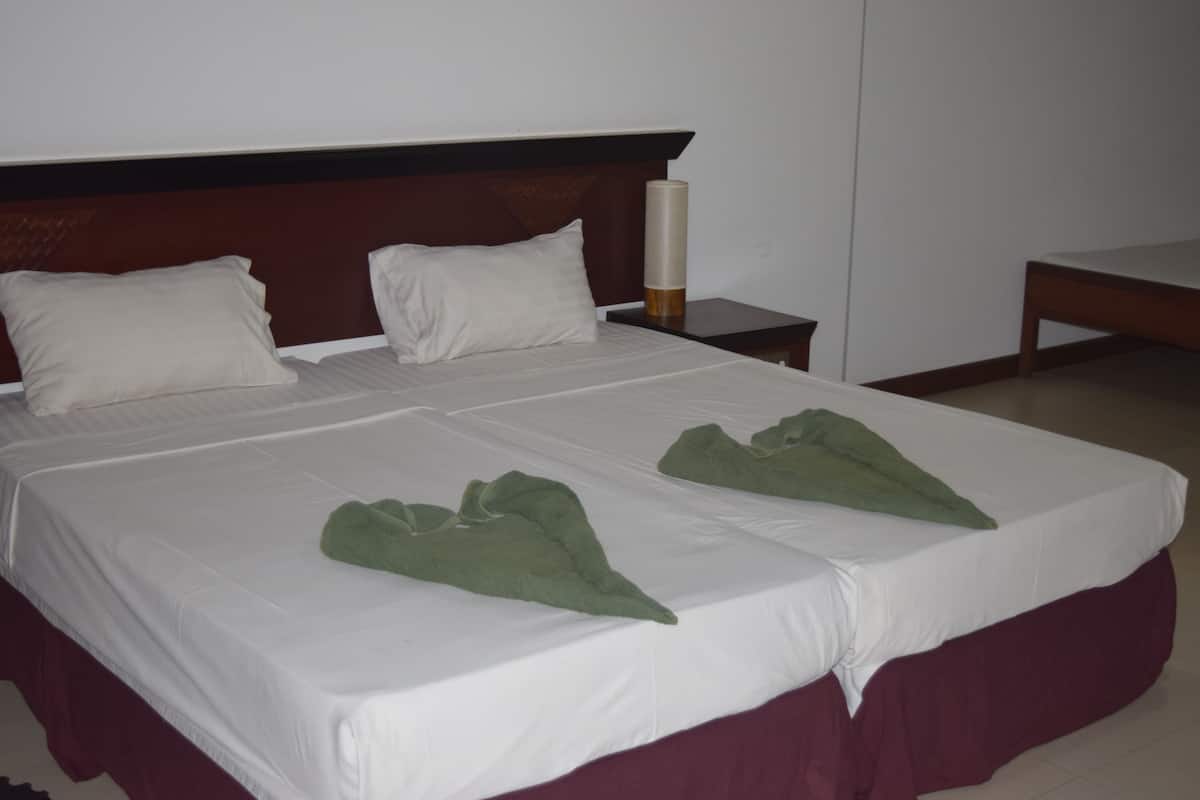 Ein ordentlich gemachtes Bett mit weißen Leinentüchern und grünen Handtüchern, ein Holz-Kopfteil und ein Nachttisch mit einer Kerze.