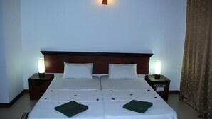 A double bed with two pillows, two bedside tables with lamps, and a bedspread with rose petals and green towels.