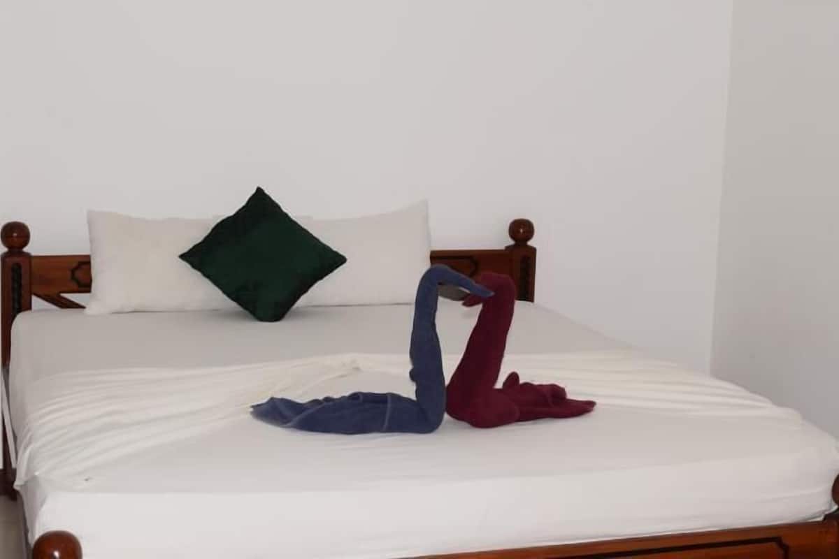 Ein Bett mit weißer Bettdecke, einem grünen Kopfkissen und zwei Handtüchern, die als Schwan drapiert sind.