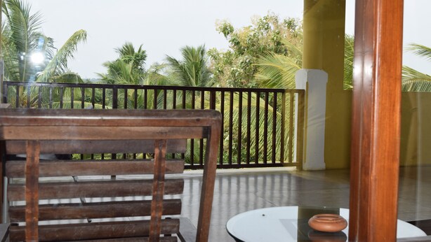 A wooden bench and a small table on a balcony with a view of palm trees and a clear sky.