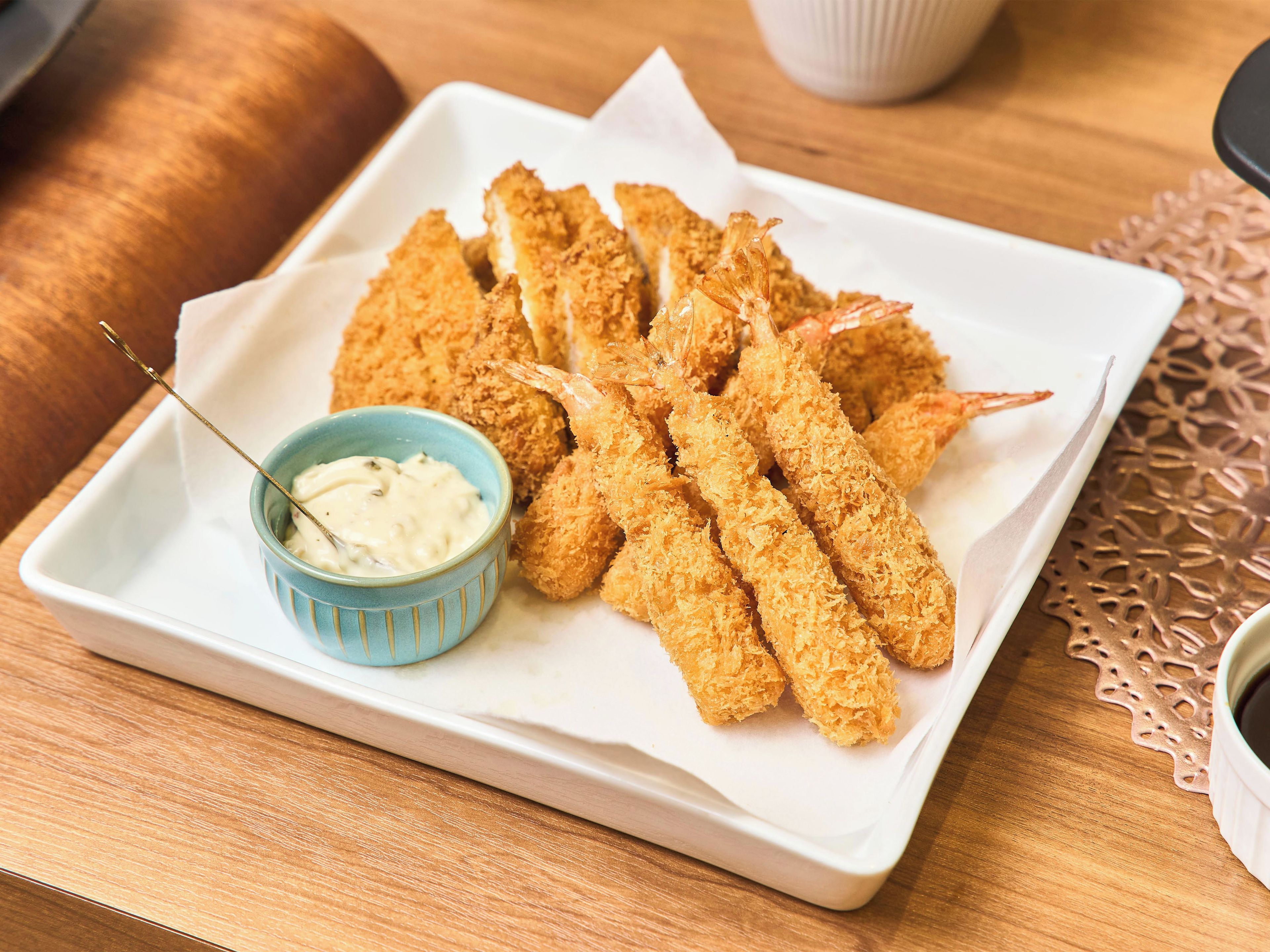 Un plato blanco rectangular con camarones enharinados y un pequeño bol azul de salsa para mojar.