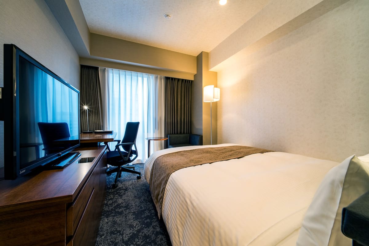 Une chambre d’hôtel équipée d’un lit, d’un bureau, d’une chaise, d’une télévision et d’une lampe.