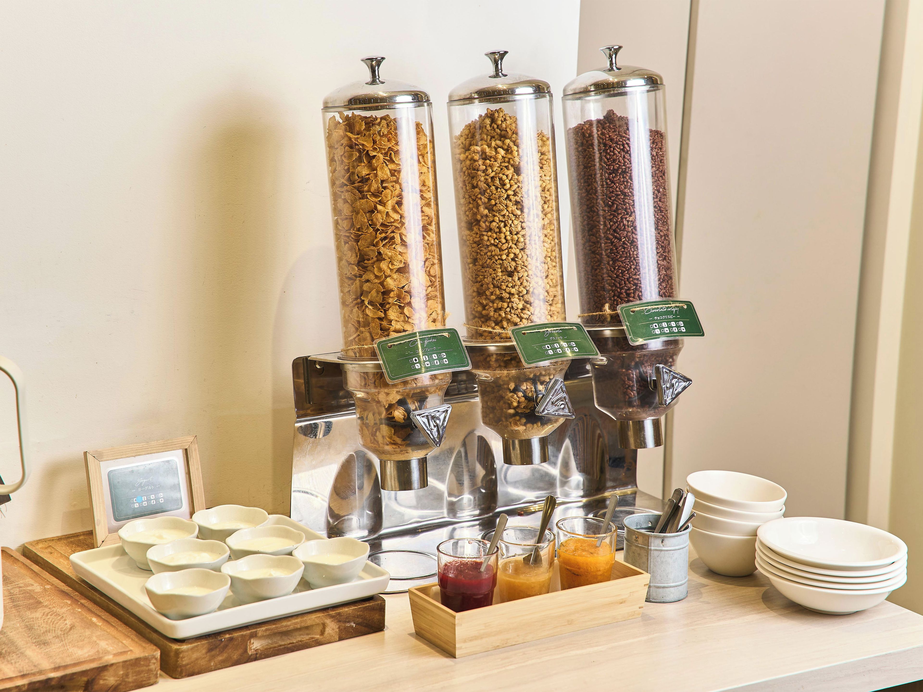 A breakfast buffet with cereal, granola, and coffee dispensers, bowls, and glasses.