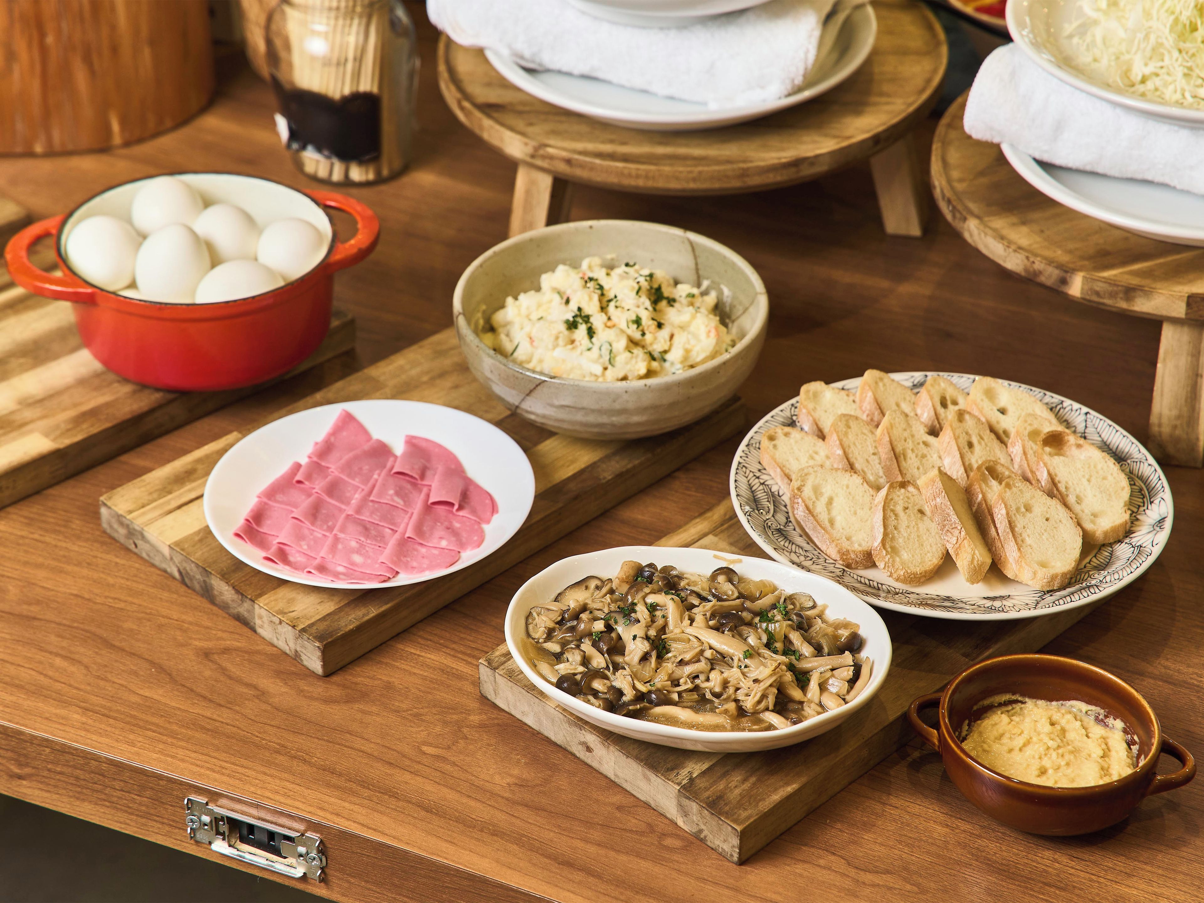 A wooden table with various food items including eggs, ham, mushrooms, and bread.