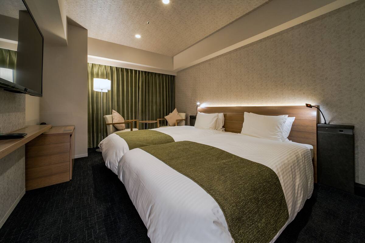 Une chambre d’hôtel avec deux lits, un bureau, une télévision et une lampe.
