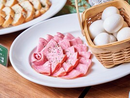 Une assiette de tranches de jambon aux herbes, un panier d’œufs et une assiette de pain.