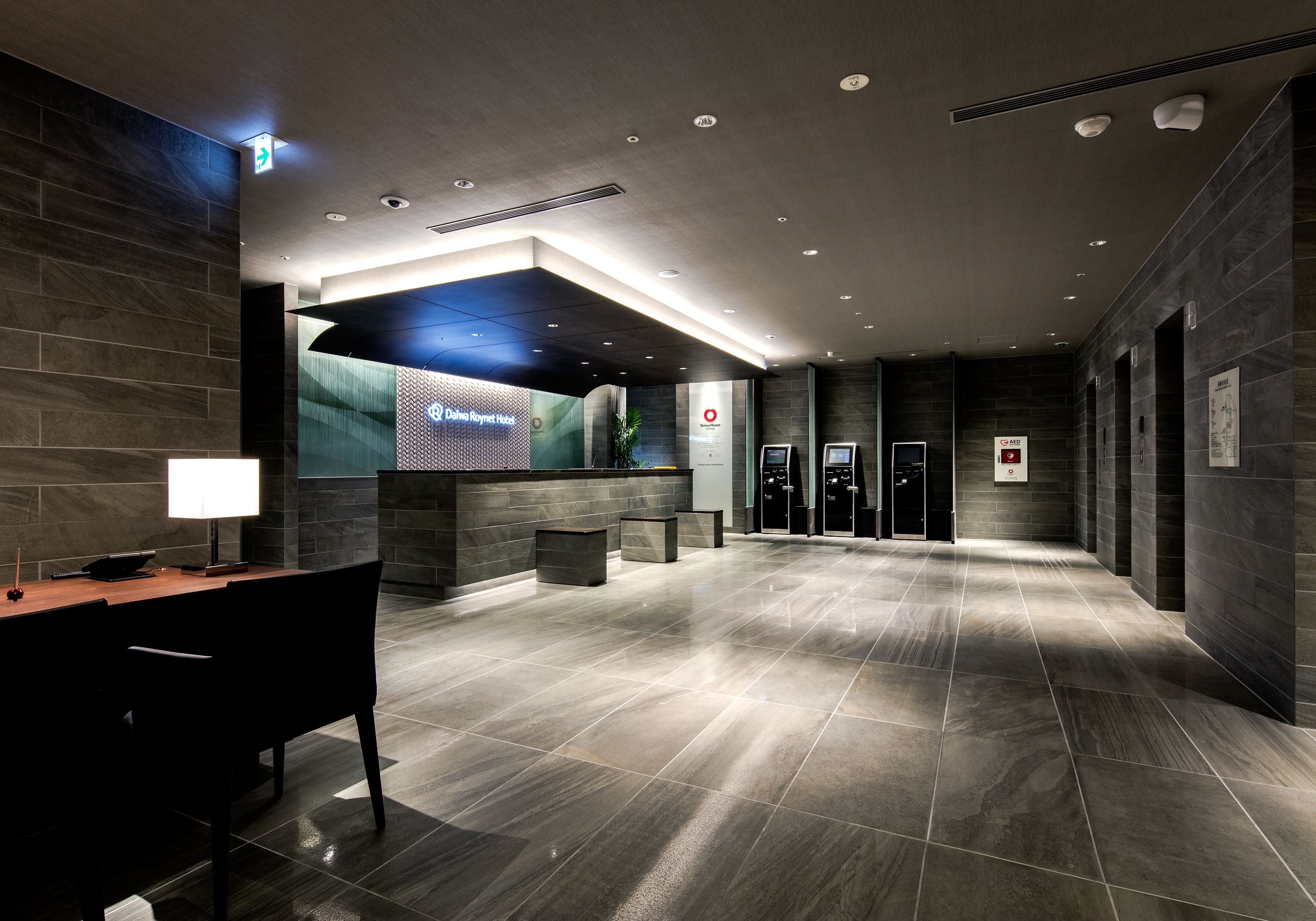 A modern hotel lobby with a reception desk, seating area, and elevators.