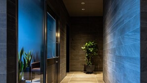 A modern hallway with dark tiled walls, a glass door, and a potted plant. - Daiwa Roynet Hotel Nagoya Taiko dori Side (Nagoya)
