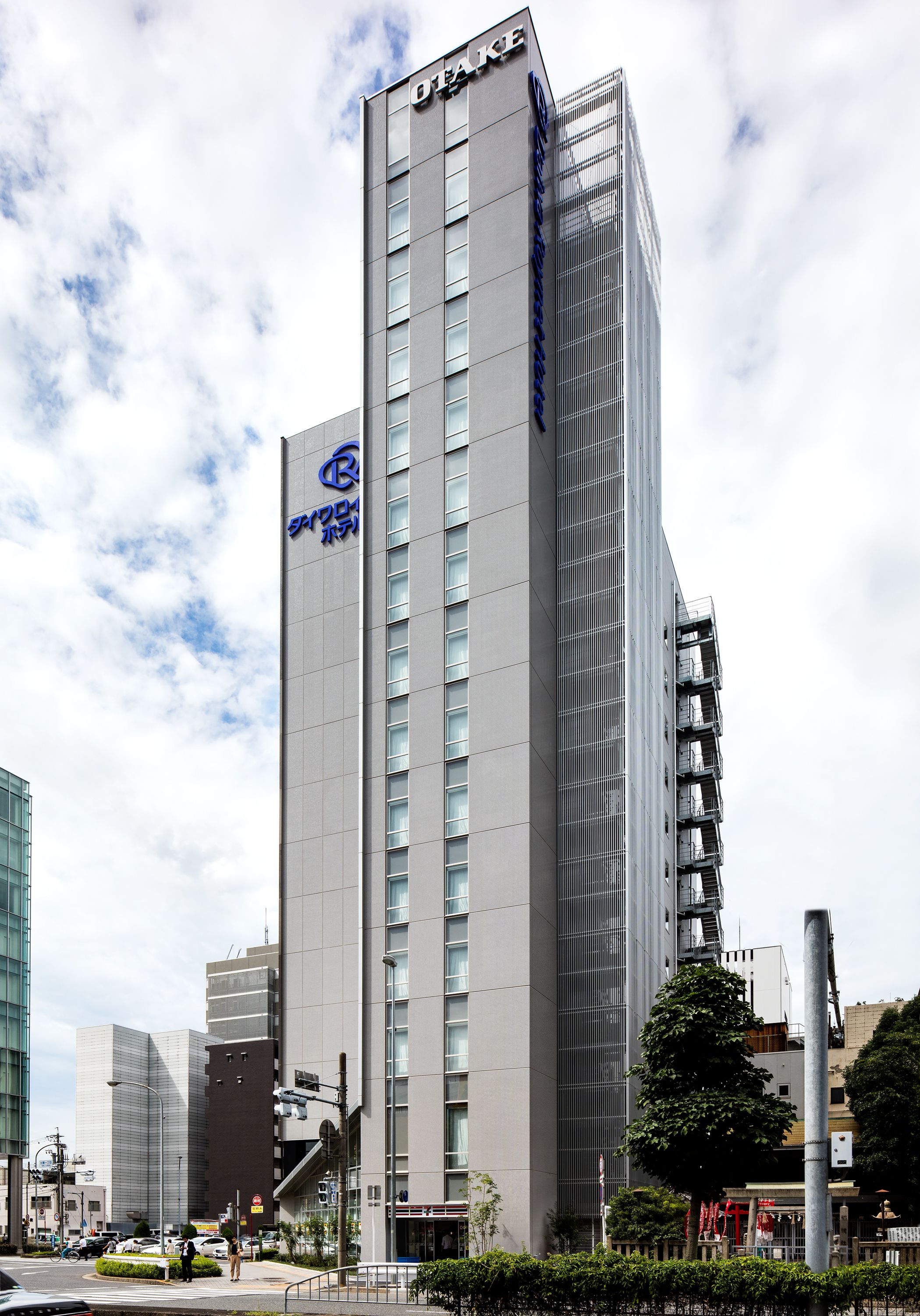 A modern high-rise building with a prominent logo on the side, surrounded by other buildings and a clear sky.