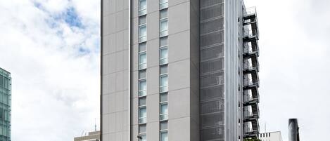 A modern high-rise building with a prominent logo on the side, surrounded by other buildings and a clear sky.