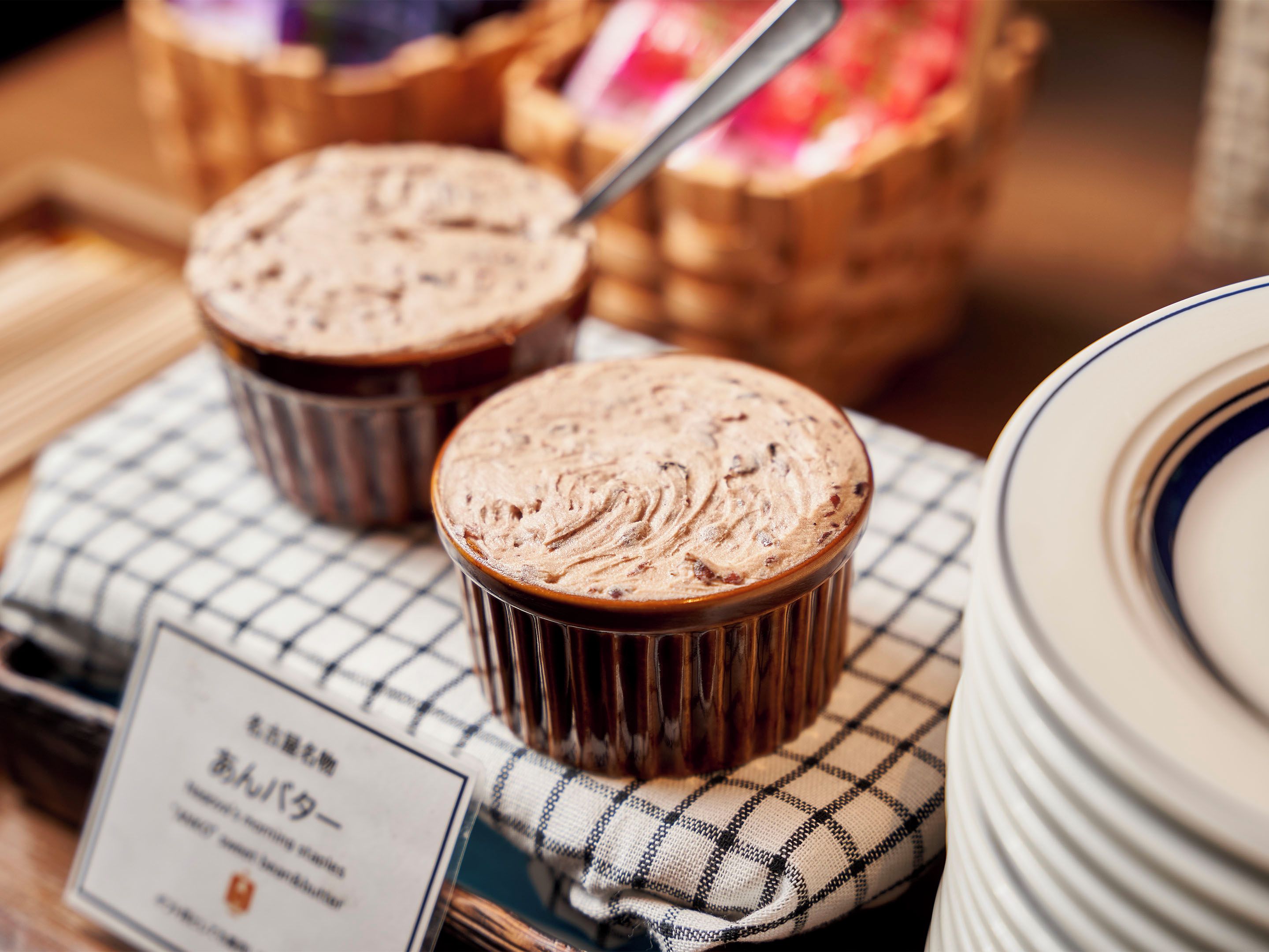 Two chocolate desserts on a checkered cloth with a spoon, a stack of plates, and a menu card.