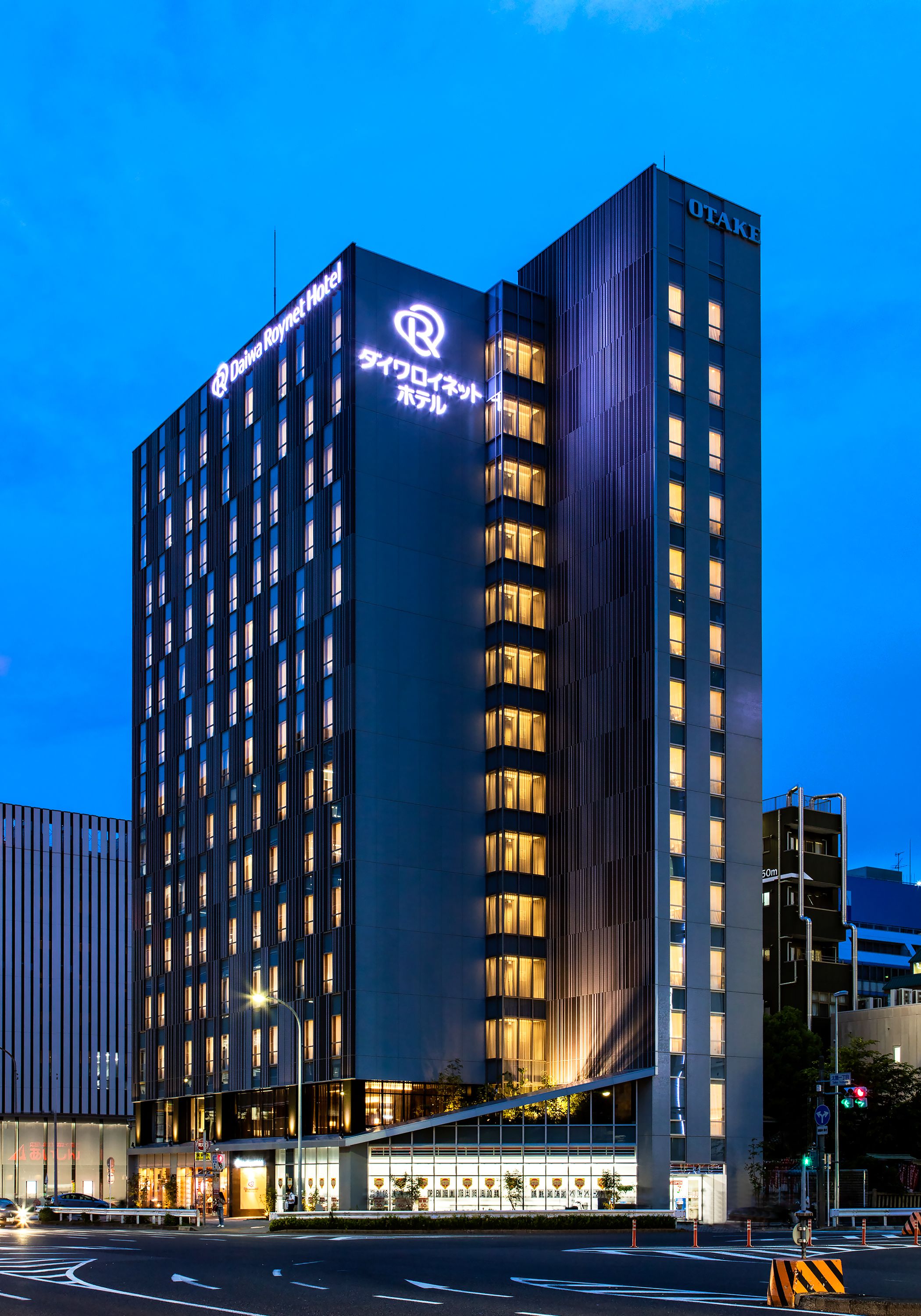 A modern hotel building with a prominent 'OTAKI' sign, multiple floors, and a well-lit facade.