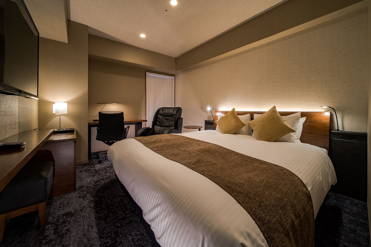 Une chambre d’hôtel avec un grand lit, un bureau, une chaise, une télévision et une table de chevet avec une lampe.