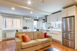 Una cocina moderna con refrigerador de acero inoxidable, gabinetes blancos y un sofá beige con cojines.